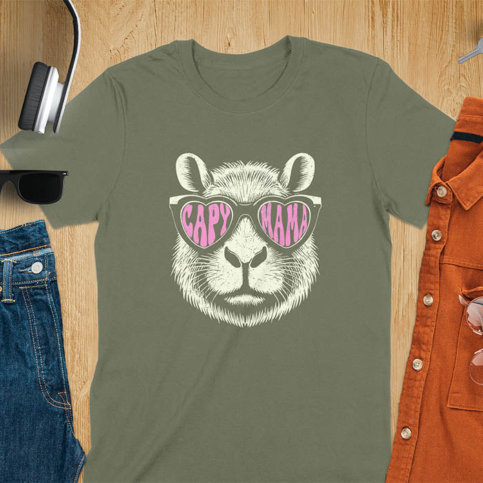 A t-shirt featuring a capybara face with pink heart-shaped sunglasses that spell CAPY MAMA. Below the capybara, Meagan is written in a pink, script font. This vintage mama shirt design is a retro mom tee-shirt perfect for mama mom life. A trendy mama tee for an expecting mom or pregnant mom gift, ideal for a pregnancy announce or pregnancy reveal. A great mom gift hers or mother days gift, or a new mom gift for a gift for wife. Personalization is available by changing the Meagan name.