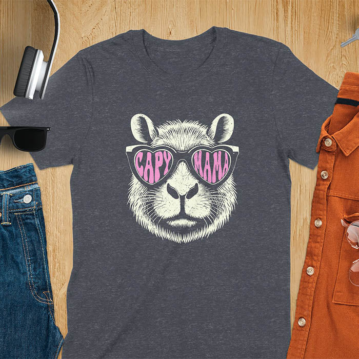 A t-shirt featuring a capybara face with pink heart-shaped sunglasses that spell CAPY MAMA. Below the capybara, Meagan is written in a pink, script font. This vintage mama shirt design is a retro mom tee-shirt perfect for mama mom life. A trendy mama tee for an expecting mom or pregnant mom gift, ideal for a pregnancy announce or pregnancy reveal. A great mom gift hers or mother days gift, or a new mom gift for a gift for wife. Personalization is available by changing the Meagan name.