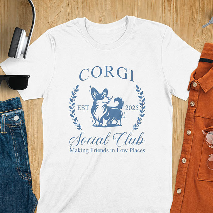 Our charming Corgi Social Club t-shirt features a delightful illustration of a corgi surrounded by laurel branches, with playful text that reads CORGI Social Club and Making friends in low places.