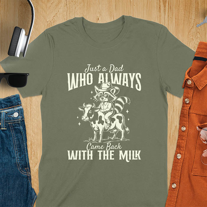 A t-shirt with a raccoon wearing a cowboy hat and sunglasses, riding a cow. Text: Just a Dad WHO ALWAYS above and Came Back WITH THE MILK below. This funny raccoon shirt features funny graphics, a dad t shirt for a funny fathers day or fathers day gift. A funny shirt for dad or gift for dad, a husband gift or father in law gifts. Could be used for a dad announcement, expectant dad, or godfather proposal.