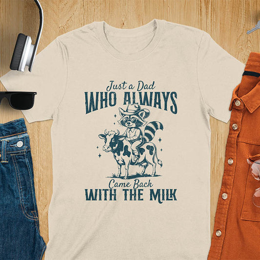 A t-shirt with a raccoon wearing a cowboy hat and sunglasses, riding a cow. Text: Just a Dad WHO ALWAYS above and Came Back WITH THE MILK below. This funny raccoon shirt features funny graphics, a dad t shirt for a funny fathers day or fathers day gift. A funny shirt for dad or gift for dad, a husband gift or father in law gifts. Could be used for a dad announcement, expectant dad, or godfather proposal.