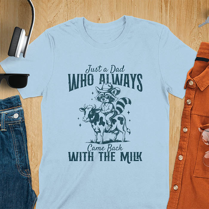 A t-shirt with a raccoon wearing a cowboy hat and sunglasses, riding a cow. Text: Just a Dad WHO ALWAYS above and Came Back WITH THE MILK below. This funny raccoon shirt features funny graphics, a dad t shirt for a funny fathers day or fathers day gift. A funny shirt for dad or gift for dad, a husband gift or father in law gifts. Could be used for a dad announcement, expectant dad, or godfather proposal.