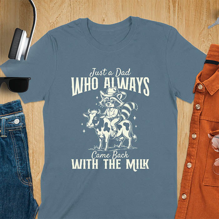 A t-shirt with a raccoon wearing a cowboy hat and sunglasses, riding a cow. Text: Just a Dad WHO ALWAYS above and Came Back WITH THE MILK below. This funny raccoon shirt features funny graphics, a dad t shirt for a funny fathers day or fathers day gift. A funny shirt for dad or gift for dad, a husband gift or father in law gifts. Could be used for a dad announcement, expectant dad, or godfather proposal.