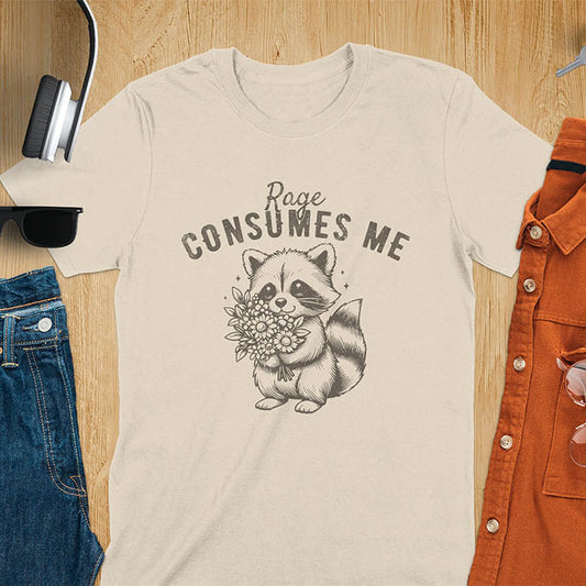 A t-shirt featuring a raccoon holding a bouquet of flowers. Text: Rage CONSUMES ME in a bold, arched font. This dark humor tee is a mental health meme and raccoon meme design. A weirdcore funny and weird funny shirt for a funny gag gift. A raccoon cuteness design, this is one of those shirts that go hard, a unisex and comfortable trendy tee. An animal person gift or girlfriend friend gift, a mom gift alternative.