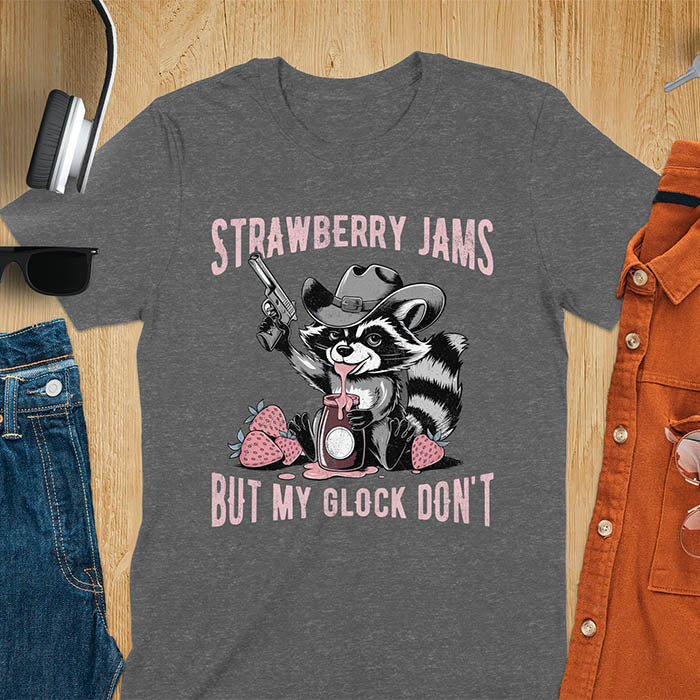 Funny raccoon t-shirt with a quirky raccoon in a cowboy hat eating strawberry jam while holding a gun. Pastel pink jam and strawberries pop against a distressed monochrome design. Text says Strawberry Jams above and But My Glock Don’t below.Funny raccoon t-shirt with a quirky raccoon in a cowboy hat eating strawberry jam while holding a gun. Pastel pink jam and strawberries pop against a distressed monochrome design. Text says Strawberry Jams above and But My Glock Don’t below.