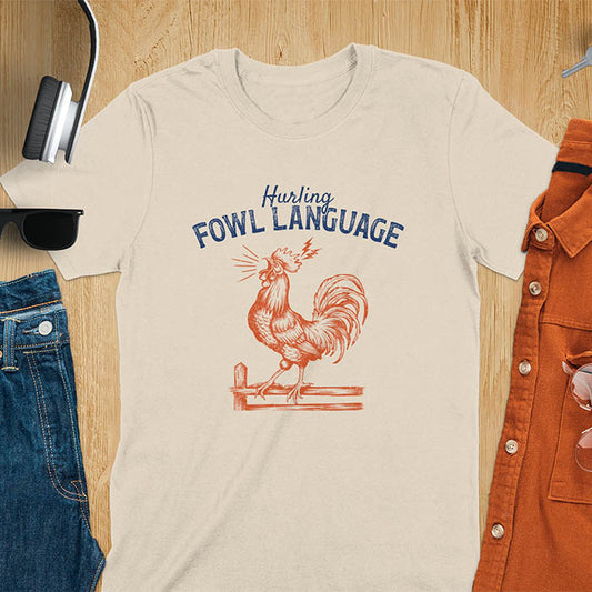 Vintage t-shirt with line art drawing of a chicken rooster standing on a fence in a farm crowing with exaggerated open beak. The design gives a fun and quirky vibe. Text says hurling fowl language.