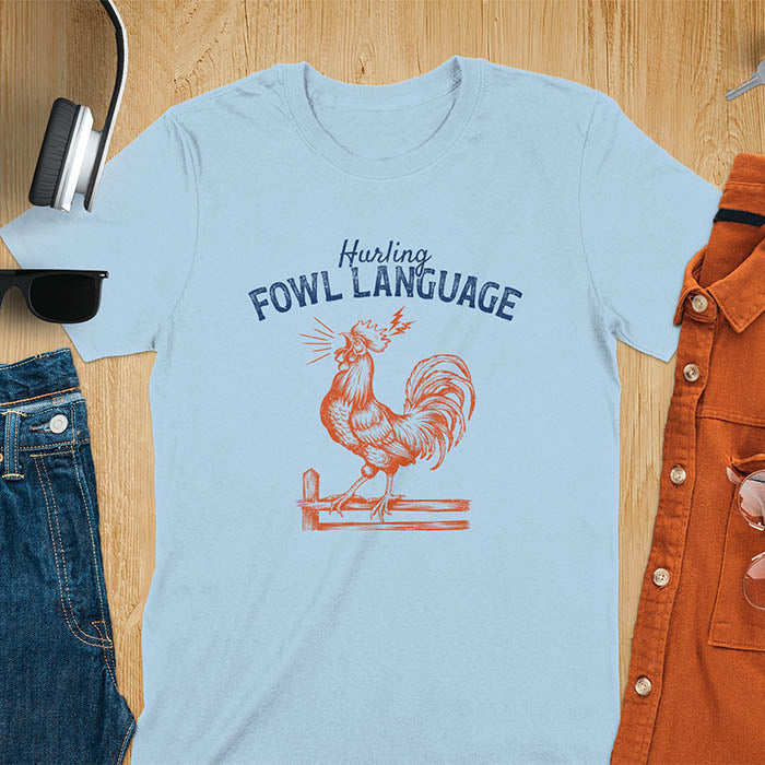Vintage t-shirt with line art drawing of a chicken rooster standing on a fence in a farm crowing with exaggerated open beak. The design gives a fun and quirky vibe. Text says hurling fowl language.