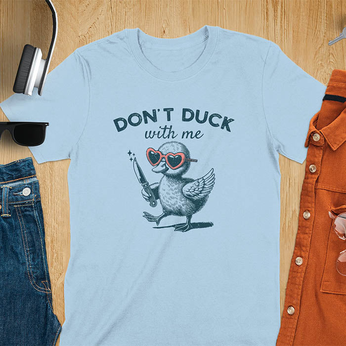 A T-shirt with a cartoon duck wearing heart-shaped sunglasses and holding a knife. The text above reads DON'T DUCK with me. The design is humorous and edgy, combining playful imagery with a bold statement.