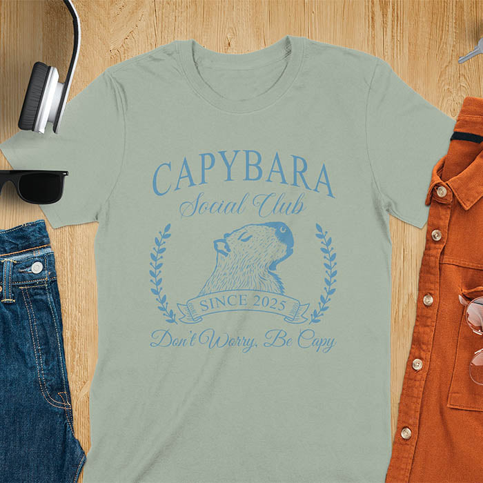 A capybara illustration within a laurel wreath and banner that reads Capybara Social Club Since 2025 and Don't Worry, Be Capy. A retro-inspired design.