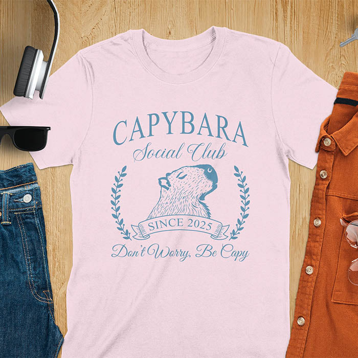 A capybara illustration within a laurel wreath and banner that reads Capybara Social Club Since 2025 and Don't Worry, Be Capy. A retro-inspired design.
