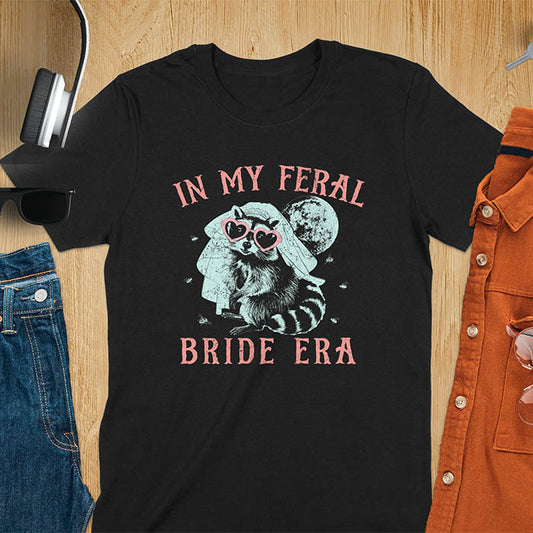 A raccoon wearing heart-shaped sunglasses and a bride's veil, with the moon in the background. Text reads In My Feral Bride Era.