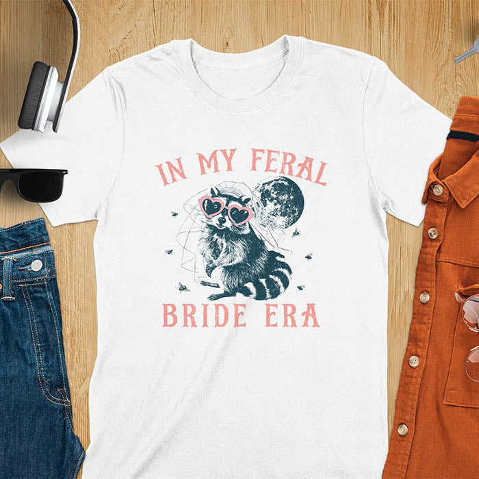 A raccoon wearing heart-shaped sunglasses and a bride's veil, with the moon in the background. Text reads In My Feral Bride Era.