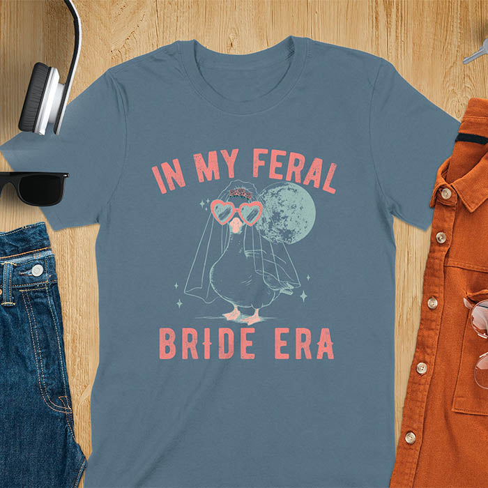 A goose standing, wearing heart-shaped sunglasses and a bride's veil. Moon in the upper right background. Retro-style text reads In My Feral on top Bride Era at bottom. Whimsical image.