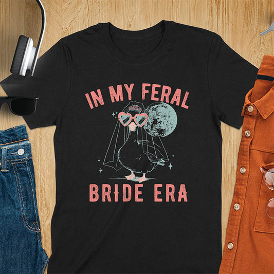 A goose standing, wearing heart-shaped sunglasses and a bride's veil. Moon in the upper right background. Retro-style text reads In My Feral on top Bride Era at bottom. Whimsical image.