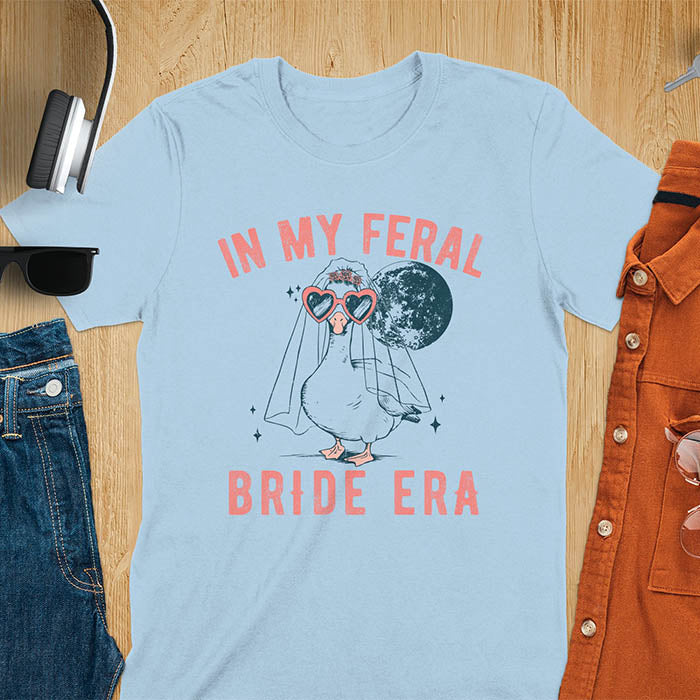 A goose standing, wearing heart-shaped sunglasses and a bride's veil. Moon in the upper right background. Retro-style text reads In My Feral on top Bride Era at bottom. Whimsical image.