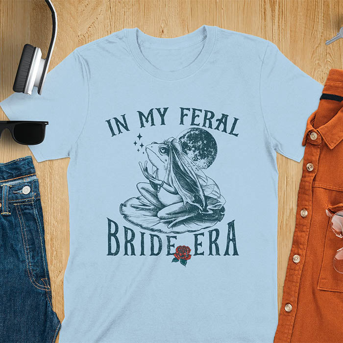 A vintage-style frog wearing a bride veil, croaking to the sky from a lily pad with a moon in the background. Text reads In My Feral Bride Era.