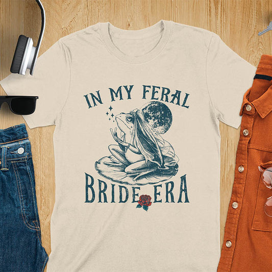 A vintage-style frog wearing a bride veil, croaking to the sky from a lily pad with a moon in the background. Text reads In My Feral Bride Era.