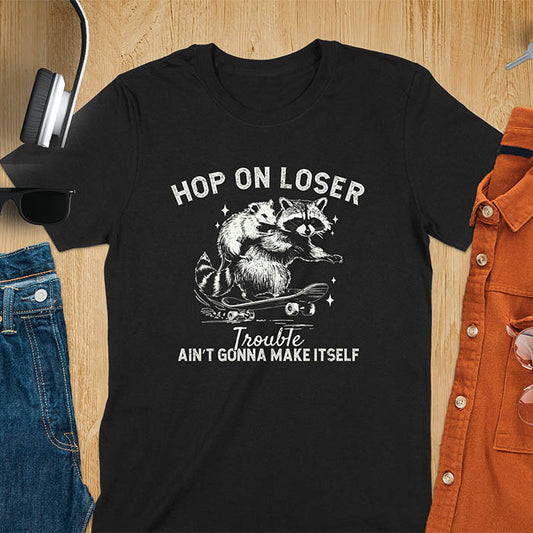 A raccoon riding a skateboard with an opossum on its back. Text reads Hop On Loser and Trouble Ain't Gonna Make Itself.