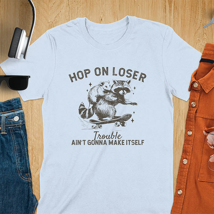A raccoon riding a skateboard with an opossum on its back. Text reads Hop On Loser and Trouble Ain't Gonna Make Itself.