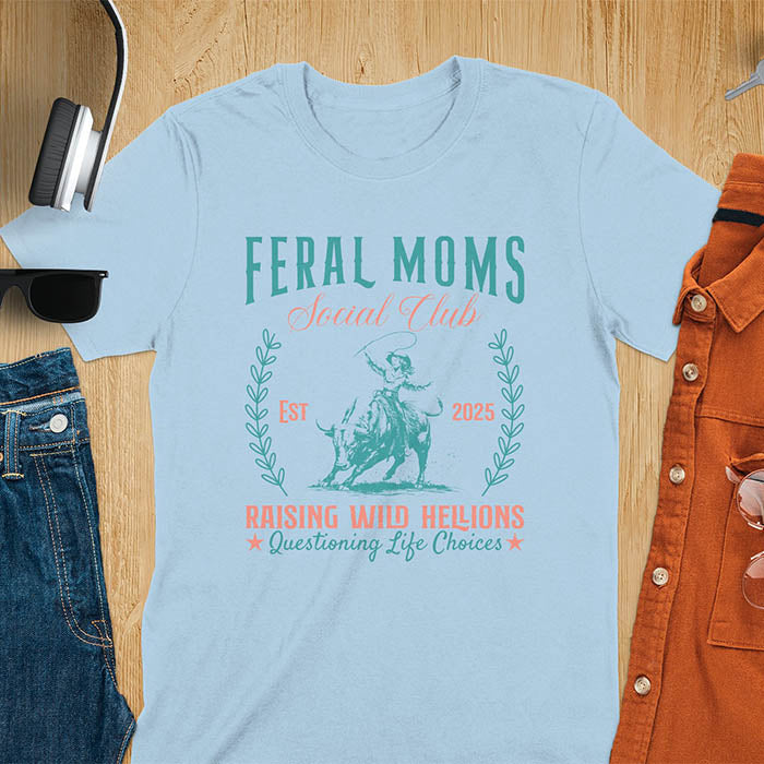 A t-shirt with a cowgirl riding a bucking bull. Text: Feral Moms SOCIAL CLUB above and Raising HELLIONS, questioning life choices below. This unhinged t-shirts design features a cowgirl mom on a rodeo bucking bull, a weird meme shirt for a feral mom gift. A retro inspired design, one of those shirts that go hard, a mama outfit or feral wife gift. A mom gift or gift for new mom for a western mama.