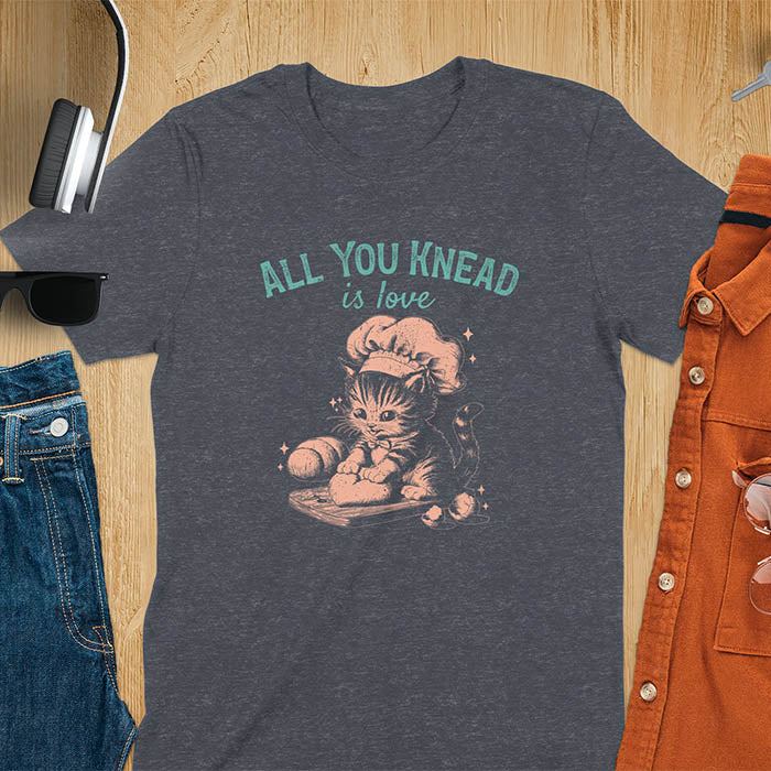 A t-shirt with a kitten wearing a chef's hat, kneading dough. Text: "ALL YOU knead" above and "is love" below. This Funny baking shirt is a Funny meme shirt showing kitten cuteness, a great cat lover gift and mom gift. An Animal lovers tshirt and cat person tee, a Pet cat owner gift. One of the Funny bakers gifts, a baker shirt gift, and a Funny cat t shirt.