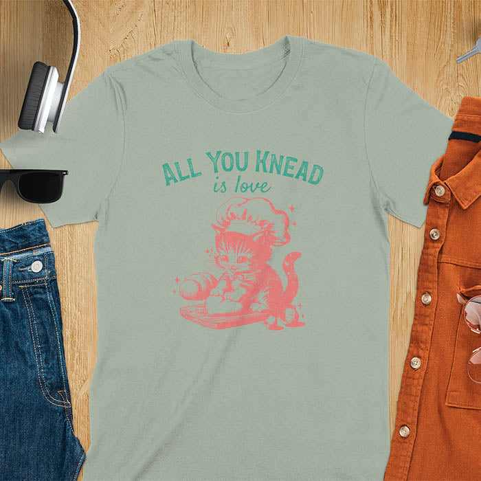 A t-shirt with a kitten wearing a chef's hat, kneading dough. Text: "ALL YOU knead" above and "is love" below. This Funny baking shirt is a Funny meme shirt showing kitten cuteness, a great cat lover gift and mom gift. An Animal lovers tshirt and cat person tee, a Pet cat owner gift. One of the Funny bakers gifts, a baker shirt gift, and a Funny cat t shirt.