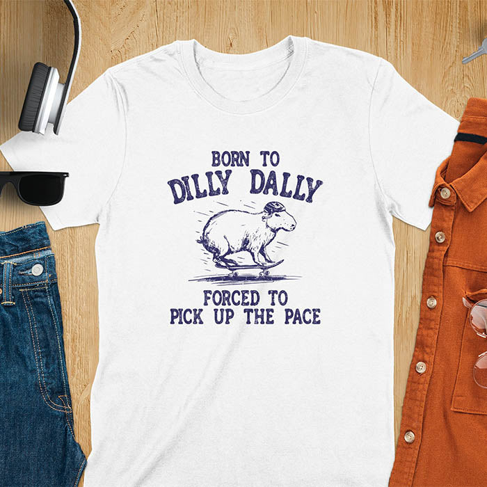A capybara skateboarding, donning a protective helmet .Above it, the words "Born to dilly dally", while below, "Forced to pick up the pace". Rendered in a charming vintage font with a faded look.