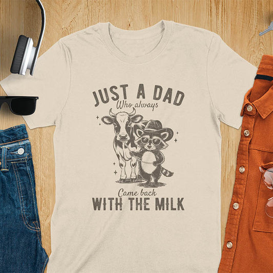 The graphic design features a cow and a cool raccoon wearing sunglasses with the text 'Just a Dad who always came back with the milk'.