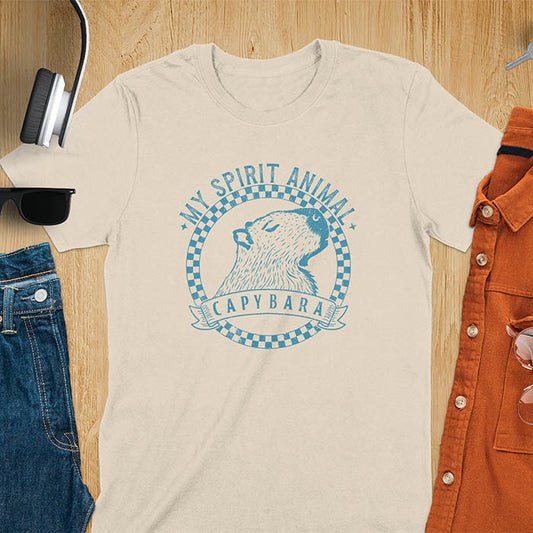 A T-shirt with a graphic of a capybara inside a checkered circle. Above the capybara, text reads "MY SPIRIT ANIMAL," and below, a banner says "CAPYBARA."
