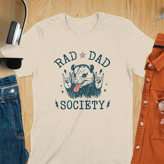 A t-shirt with an opossum sticking its tongue out and giving rock-on hand signs. Text: "RAD DAD" above and "SOCIETY" below. This rad dad society tee is for the cool dad club. A dad humor gift and cool dad tee-shirt, a daddie's t shirt or dad birthday shirt. A first father's day or fathers day gifts, a new daddy gift or gift for daddie. A pet dad gift for a husband outfit.
