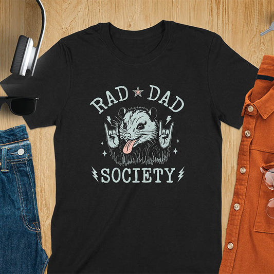 A t-shirt with an opossum sticking its tongue out and giving rock-on hand signs. Text: "RAD DAD" above and "SOCIETY" below. This rad dad society tee is for the cool dad club. A dad humor gift and cool dad tee-shirt, a daddie's t shirt or dad birthday shirt. A first father's day or fathers day gifts, a new daddy gift or gift for daddie. A pet dad gift for a husband outfit.
