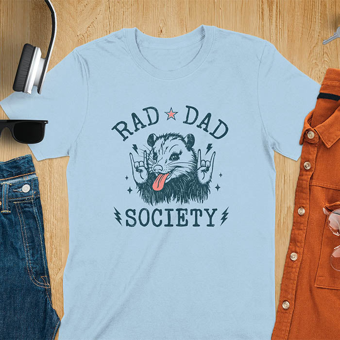 A t-shirt with an opossum sticking its tongue out and giving rock-on hand signs. Text: "RAD DAD" above and "SOCIETY" below. This rad dad society tee is for the cool dad club. A dad humor gift and cool dad tee-shirt, a daddie's t shirt or dad birthday shirt. A first father's day or fathers day gifts, a new daddy gift or gift for daddie. A pet dad gift for a husband outfit.
