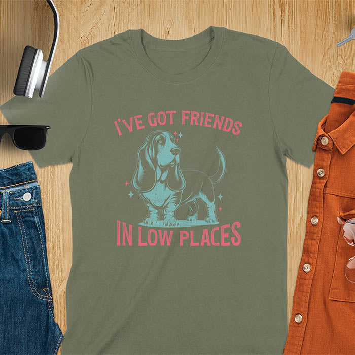 This retro dog shirt features a vintage dog tee design of a basset hound standing proudly, tail high, and gazing to the side. Text reads “I’ve got friends” above and “in low places” below. A distressed texture adds charm to the shirt.