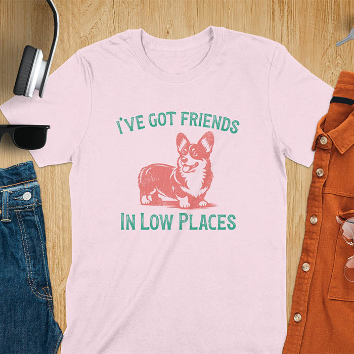 Our vintage-inspired design features a cute corgi silhouette with facial details. Text above it says 'I've Got Friends' and below it says ''In Low Places.' With its retro vibe and distressed texture, this tee adds a touch of nostalgia to your wardrobe.