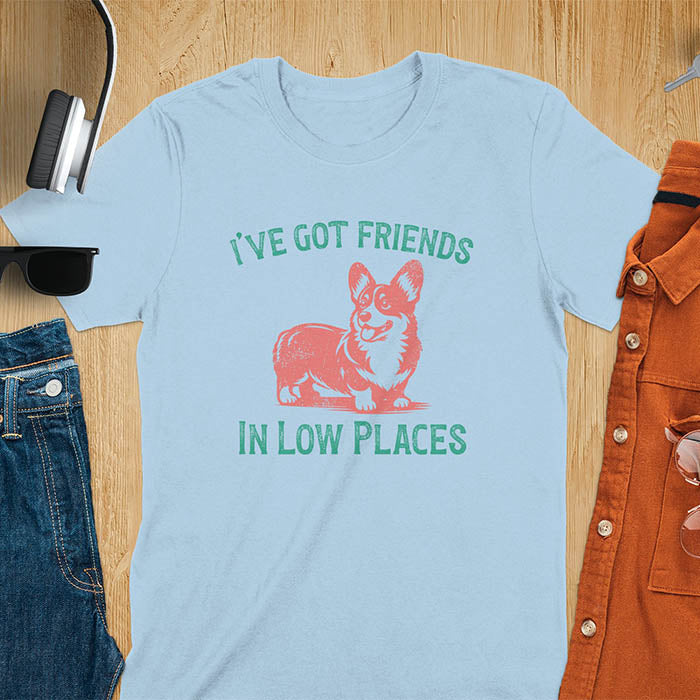 Our vintage-inspired design features a cute corgi silhouette with facial details. Text above it says 'I've Got Friends' and below it says ''In Low Places.' With its retro vibe and distressed texture, this tee adds a touch of nostalgia to your wardrobe.