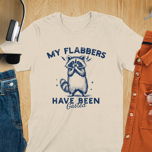 A t-shirt featuring a raccoon with wide eyes and paws covering its mouth. Text: MY FLABBERS above and HAVE BEEN Gasted below in a distressed font. This sarcastic tee-shirt features a funny raccoon with kawaiiness cuteness, a genz meme tee or anxiety tshirt. A depress meme and weirdcore memes design, a funny gag gift for sad core fans. This is one of those shirts that go hard, a trash panda design.