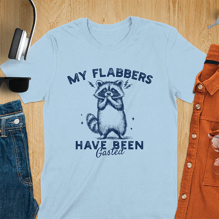 A t-shirt featuring a raccoon with wide eyes and paws covering its mouth. Text: MY FLABBERS above and HAVE BEEN Gasted below in a distressed font. This sarcastic tee-shirt features a funny raccoon with kawaiiness cuteness, a genz meme tee or anxiety tshirt. A depress meme and weirdcore memes design, a funny gag gift for sad core fans. This is one of those shirts that go hard, a trash panda design.
