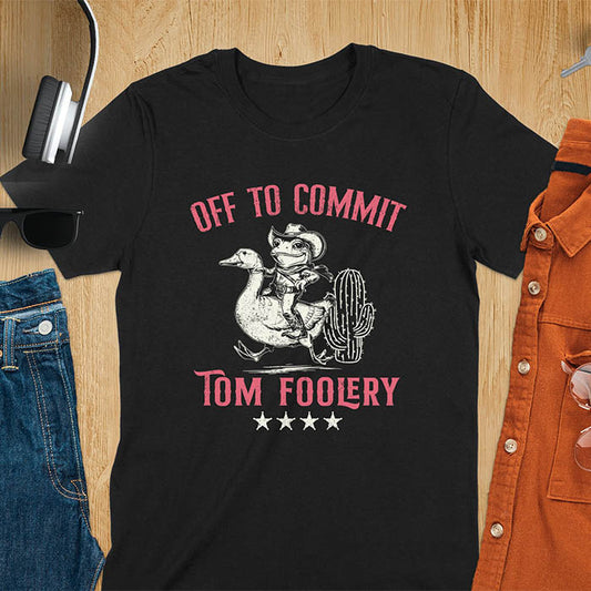 A t-shirt with a frog dressed as a rodeo cowboy riding a goose. Text: "Off To COMMIT" above and "TOM FOOLERY" below. This meme t shirt features a funny frog tee and silly funny goose, a weird graphics shirt. A funny genz meme and unhinged tee-shirt, with rodeo cowboy and cowgirl t shirt elements. A retro aesthetic and western style gift, an animal person gift. A mom gift alternative.