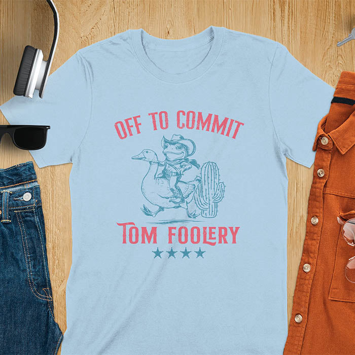 A t-shirt with a frog dressed as a rodeo cowboy riding a goose. Text: "Off To COMMIT" above and "TOM FOOLERY" below. This meme t shirt features a funny frog tee and silly funny goose, a weird graphics shirt. A funny genz meme and unhinged tee-shirt, with rodeo cowboy and cowgirl t shirt elements. A retro aesthetic and western style gift, an animal person gift. A mom gift alternative.