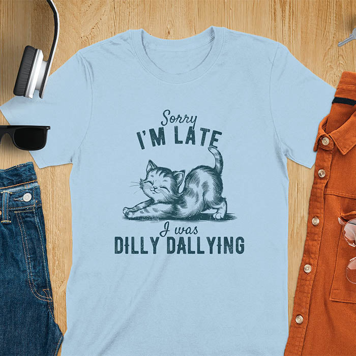 A t-shirt with a kitten stretching its back. Text: Sorry I'M LATE above and I was DILLY DALLYING below. This cat lover shirt features cat cuteness gift and kawaiiness cuteness. A sarcastic meme shirt about dilly dally, a funny genz meme with funny animals. This kawaii kitten design has vintage aesthetics, a snarky humorous tee, an animal person gift or mom gift hers. A cat mom t shirt alternative.