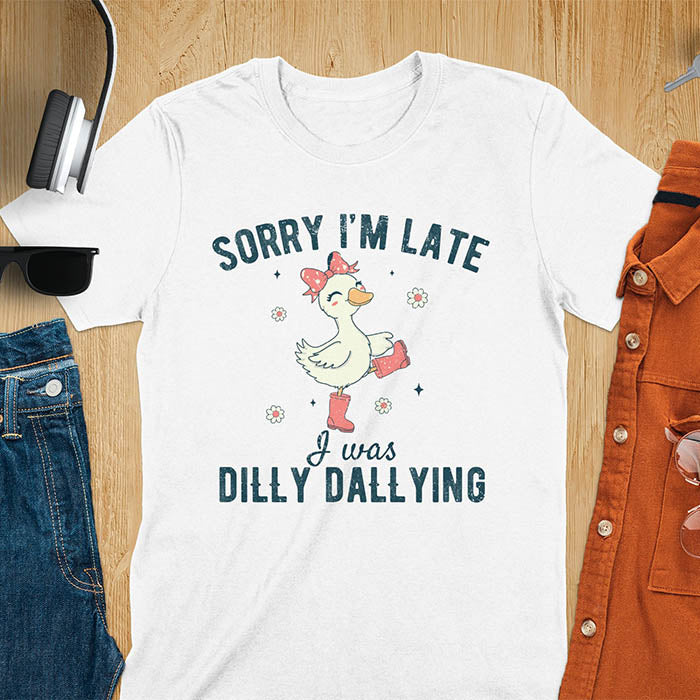 A t-shirt with a white goose wearing pink boots and a pink bow, surrounded by small flowers. Text: SORRY I'M LATE above and I was DILLY DALLYING below. This cute geese t shirt features goose cuteness and kawaiiness cuteness. A snarky humorous and sarcastic meme shirt about dilly dallying. A funny genz meme with funny animals and spring flowers. This silly funny goose design has vintage aesthetics and is an animal person gift or mom gift.