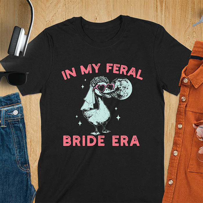 A goose standing, wearing heart-shaped sunglasses and a bride's veil. Moon in the upper right background. Retro-style text reads In My Feral Bride Era and Bride Era. Whimsical image.