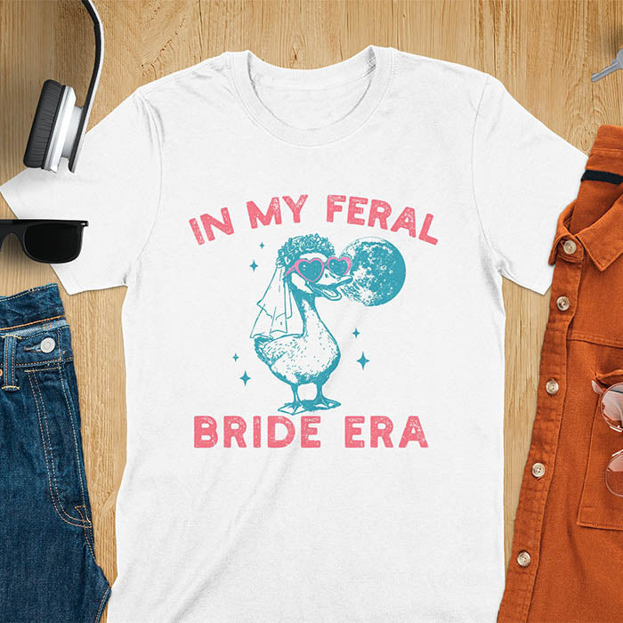 A goose standing, wearing heart-shaped sunglasses and a bride's veil. Moon in the upper right background. Retro-style text reads In My Feral Bride Era and Bride Era. Whimsical image.
