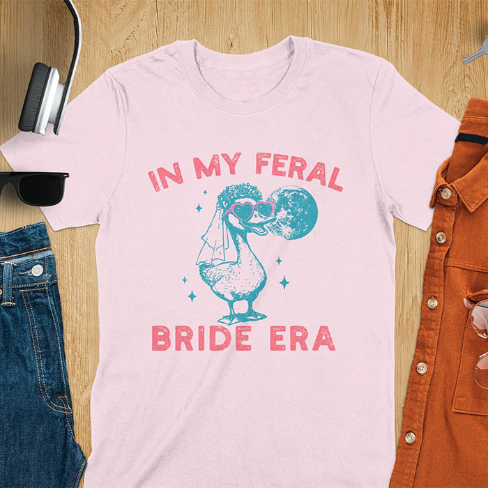 A goose standing, wearing heart-shaped sunglasses and a bride's veil. Moon in the upper right background. Retro-style text reads In My Feral Bride Era and Bride Era. Whimsical image.