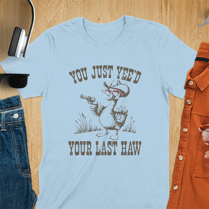 A t-shirt with a goose wearing a cowboy hat and sunglasses, holding a pistol. Text: "YOU JUST YEE'D" above and "YOUR LAST HAW" below. This funny western shirt features a silly goose shirt or goose lovers gift. A cowboy tshirt or cowgirl shirt, a western style tee and western shirt. A retro graphic tee and weirdcore tshirt, an animal person gift or animal lover gag. A mom gift alternative.