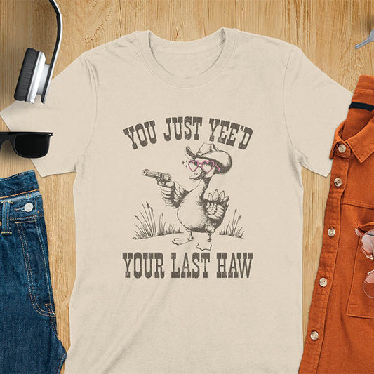 A t-shirt with a goose wearing a cowboy hat and sunglasses, holding a pistol. Text: "YOU JUST YEE'D" above and "YOUR LAST HAW" below. This funny western shirt features a silly goose shirt or goose lovers gift. A cowboy tshirt or cowgirl shirt, a western style tee and western shirt. A retro graphic tee and weirdcore tshirt, an animal person gift or animal lover gag. A mom gift alternative.