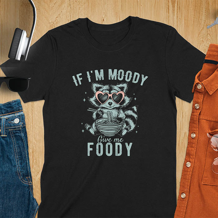 A t-shirt: raccoon in heart sunglasses with noodles. Text: "IF I'M MOODY Give me FOODY". A Funny Raccoon T-shirt, funny trash panda, Vintage Trash Panda Tee. Sarcastic Saying Tee-shirt, snarky humorous, trending funny shirt, meme t shirt, Gag Gift. Features kawaiiness cuteness. Great gift for animal person, Animal Lover Tshirt, mom. Retro aesthetic tee.