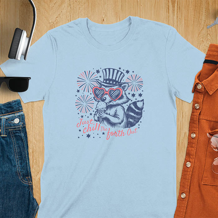 A t-shirt with a raccoon in a patriotic top hat & heart sunglasses, holding an ice cream cone. Fireworks burst around it. Text: "JUST CHILL THE FOURTH OUT". This raccoon cuteness tee is a funny 4th of July fourth of july shirt for chill the 4th out. A fireworks shirt, patriotic merica tee & freedom t shirt for independence day. Has vintage aesthetics, a funny patriot animal person gift or mom gift among 4th of july shirts.