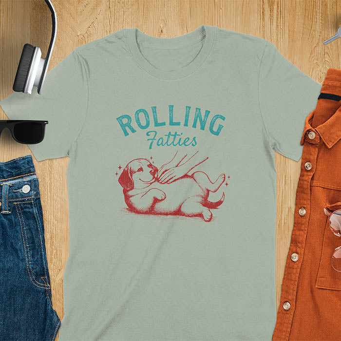 Sage colored t-shirt featuring 'Rolling Fatties' text in teal lettering above a chubby beagle dog lying on its back in red/burgundy ink sketch style