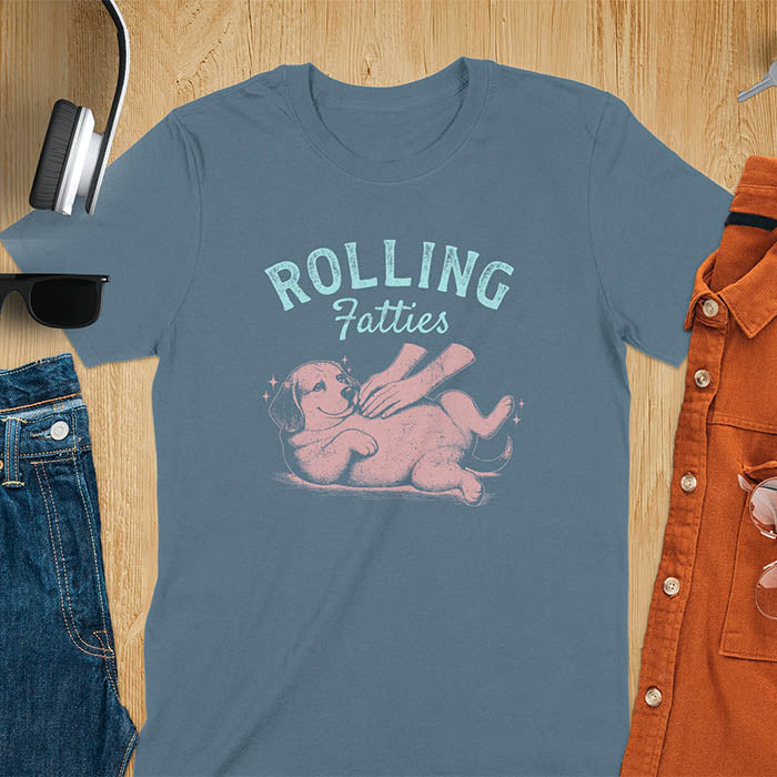 Indigo blue t-shirt featuring 'Rolling Fatties' text in teal lettering above a chubby beagle dog lying on its back in red/burgundy ink sketch style
